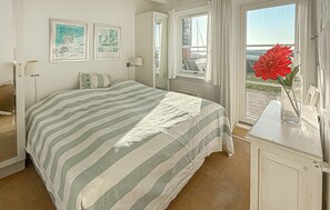 A hotel room with a bed, a window with curtains, a vase with a flower, and two framed pictures on the wall.