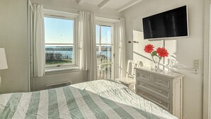 Un dormitorio con una cama, un aparador, un televisor montado en la pared y un ventanal con cortinas.