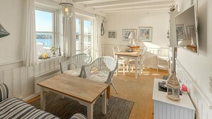 Una habitación acogedora con una mesa de madera, sillas de mimbre, un sofá a rayas y vistas al mar a través de amplios ventanales.