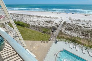Blick auf einen Strand vom Balkon mit Pool und Liegestühlen.