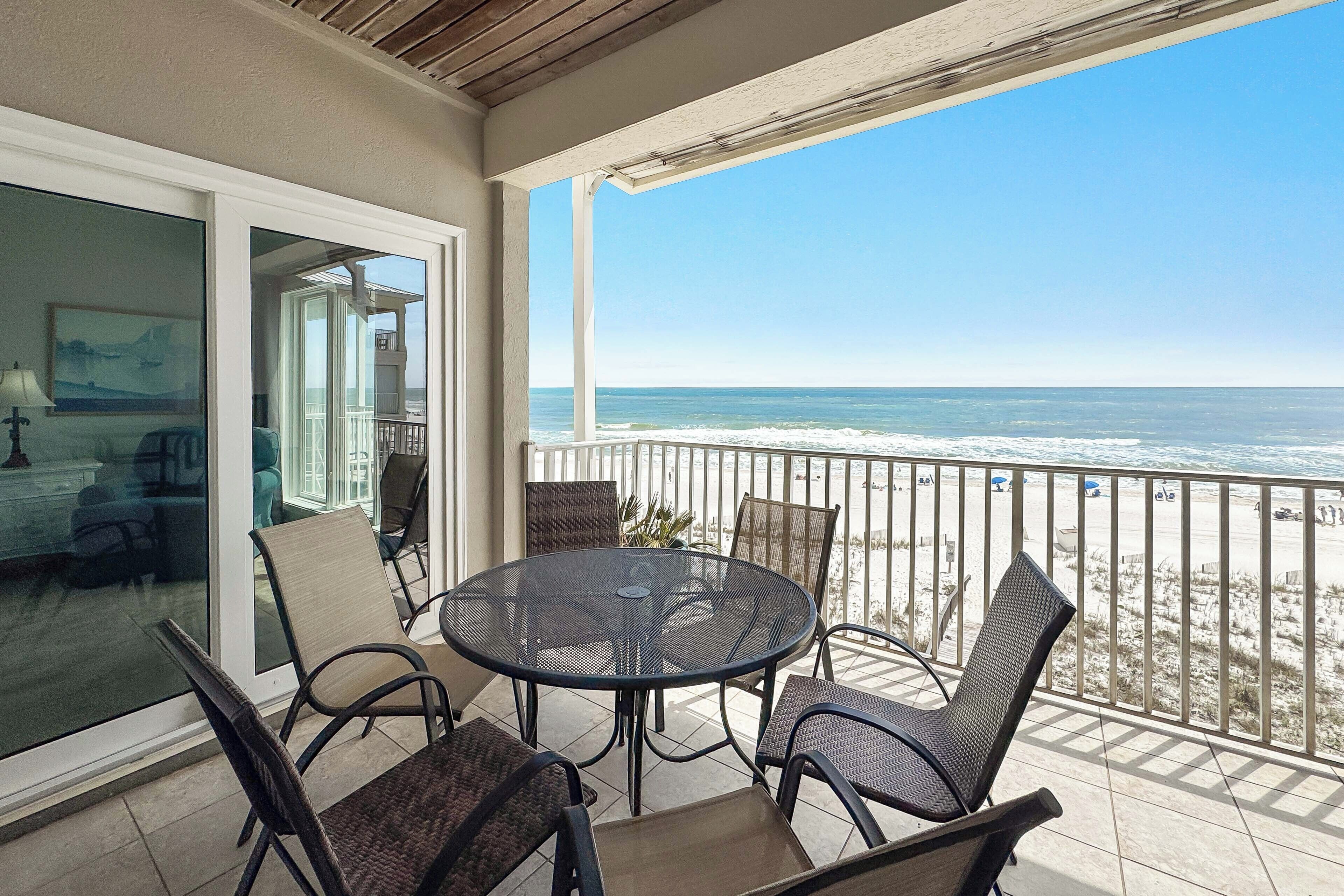 A balcony with a round table and chairs, a glass door leading to an interior room, and a view of the ocean.