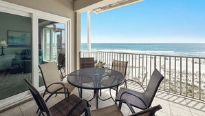 A balcony with a round table and chairs, a glass door leading to an interior room, and a view of the ocean. - Dolphin Key 3C | Beachfront | Pool | Boat Slips | My Beach Getaways (Orange Beach)