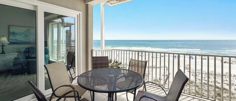 A balcony with a round table and chairs, a glass door leading to an interior room, and a view of the ocean.