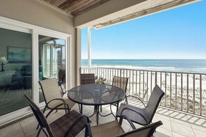 Ein Balkon mit rundem Tisch und Stühlen, eine Glastür zu einem Innenraum und Blick aufs Meer.