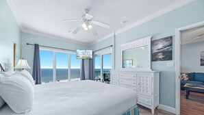 A bedroom with a large bed, a ceiling fan, a TV, a dresser, and a view of the ocean. - Dolphin Key 3C | Beachfront | Pool | Boat Slips | My Beach Getaways (Orange Beach)