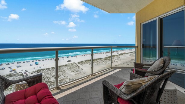 Ein Balkon mit Korbmöbeln, Blick auf den Strand und einen klaren Himmel.