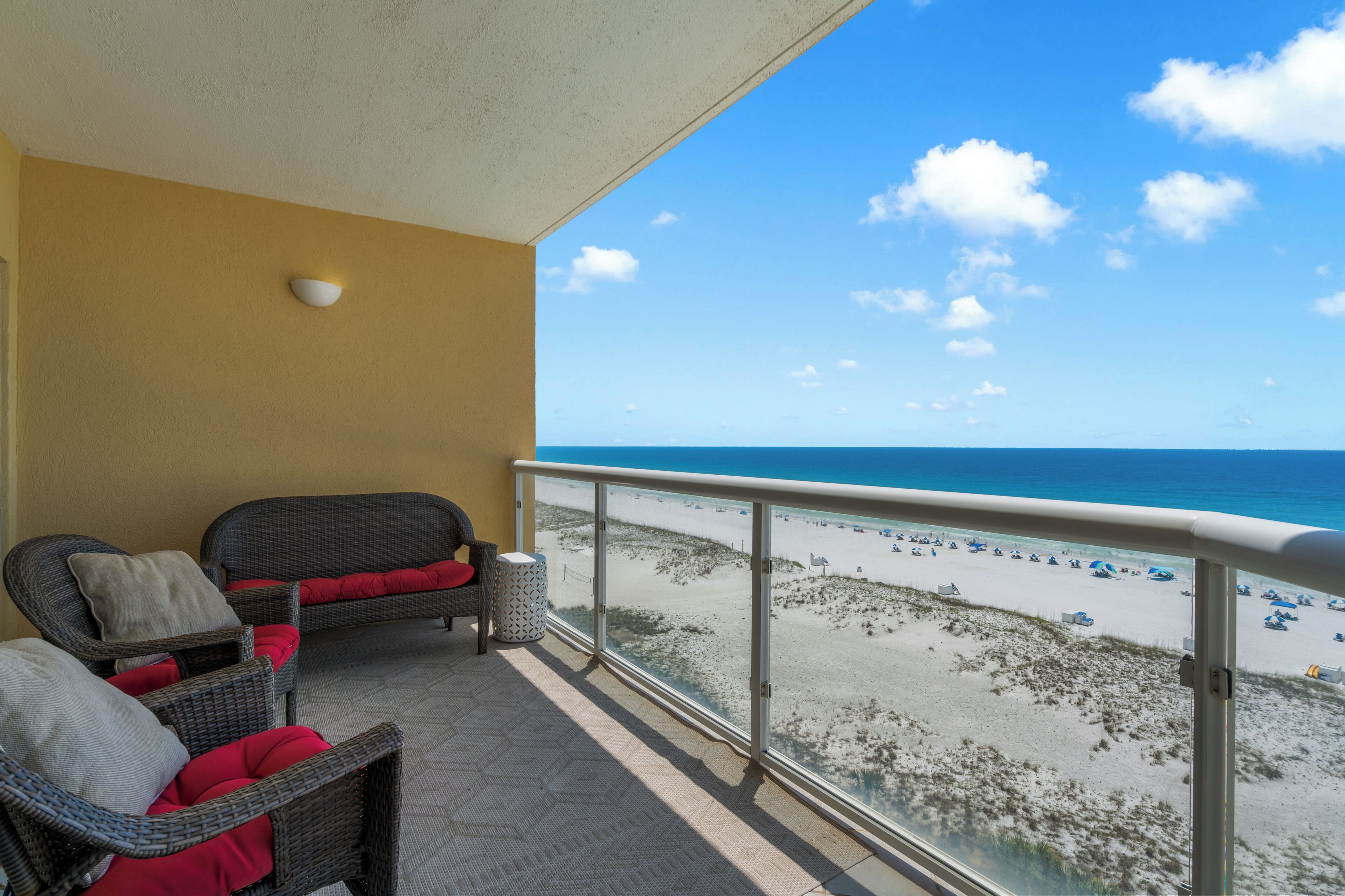 Een balkon met rieten meubilair, uitzicht op het strand en een heldere lucht.