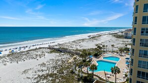 Ein Strandhotel mit Schwimmbecken, Strandsonnenschirmen und einem Pier im Hintergrund.