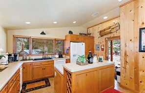 A kitchen with wooden cabinets, a refrigerator, a sink, and a countertop with various items. - Unique Lake Views for Big Groups with Hot Tub, Game Room, Fire Pit, & More (Big Bear Lake)