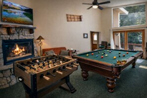 A room with a foosball table, a pool table, a fireplace, and a large window. - Unique Lake Views for Big Groups with Hot Tub, Game Room, Fire Pit, & More (Big Bear Lake)