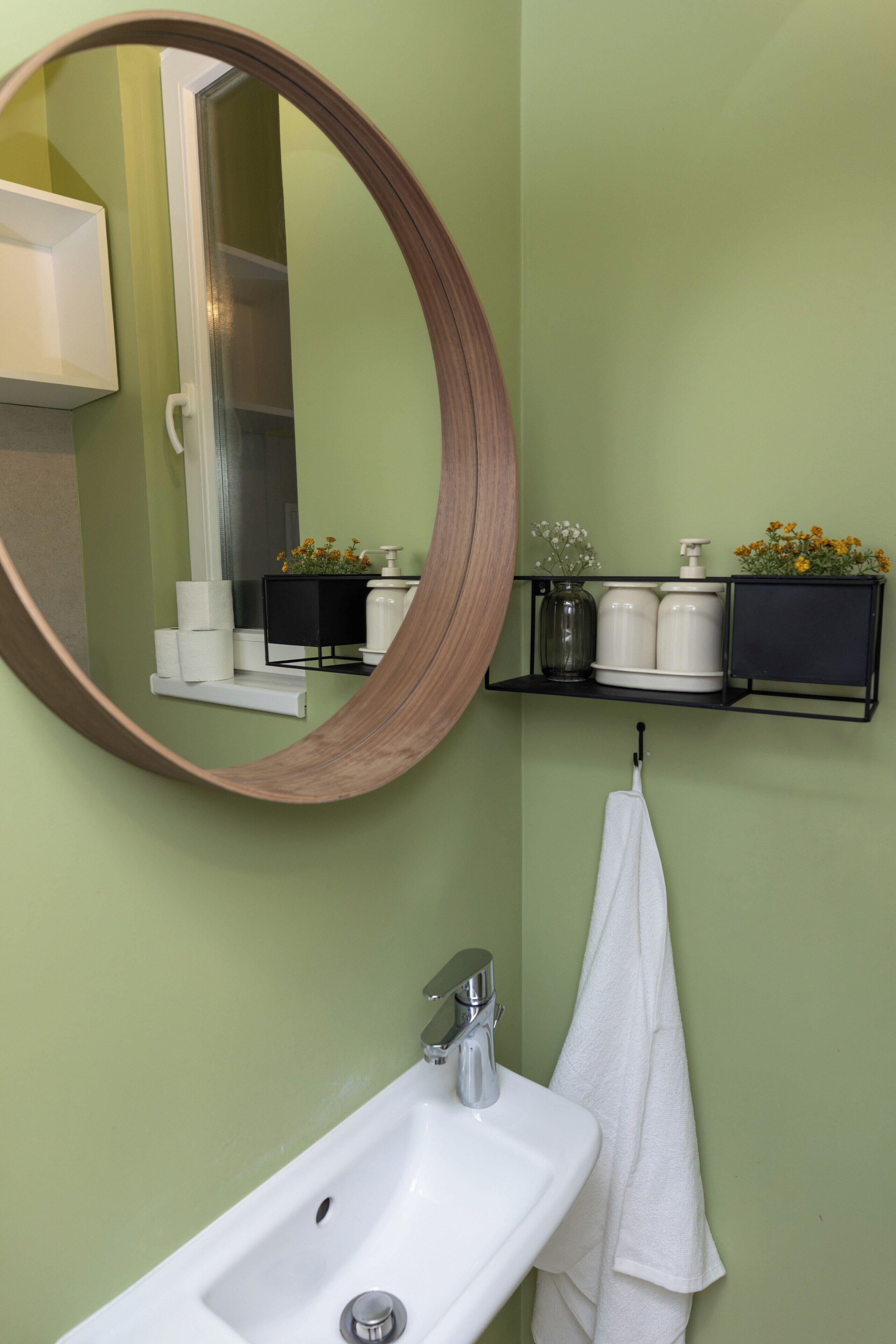A bathroom with a white sink, a mirror, a towel hanging on a rack, and a shelf with toiletries.