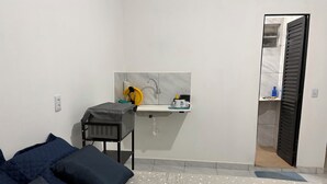 A small, modern bedroom with a bed, a bedside table, a small desk with a chair, a sink, and a mirror. - New ground floor apartment, close to the airport and city center. (Teresina)