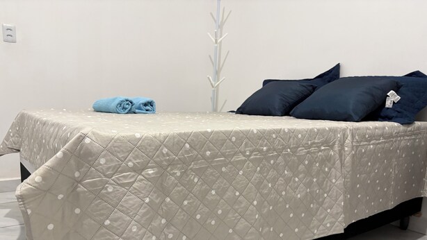 A bed with a quilted cover, a blue towel, and two dark pillows. - New ground floor apartment, close to the airport and city center. (Teresina)