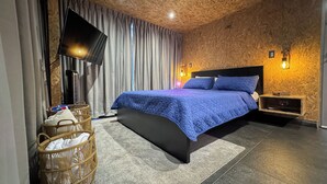 A modern bedroom with a large bed, a flat-screen TV, a wall-mounted heater, and a wicker basket. - Cozy Cabin, Jacuzzi, AC, Fireplace and Hot water. (Jarabacoa)