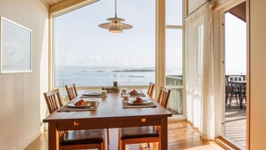 A dining area with a table set for two, overlooking a scenic view of the sea.