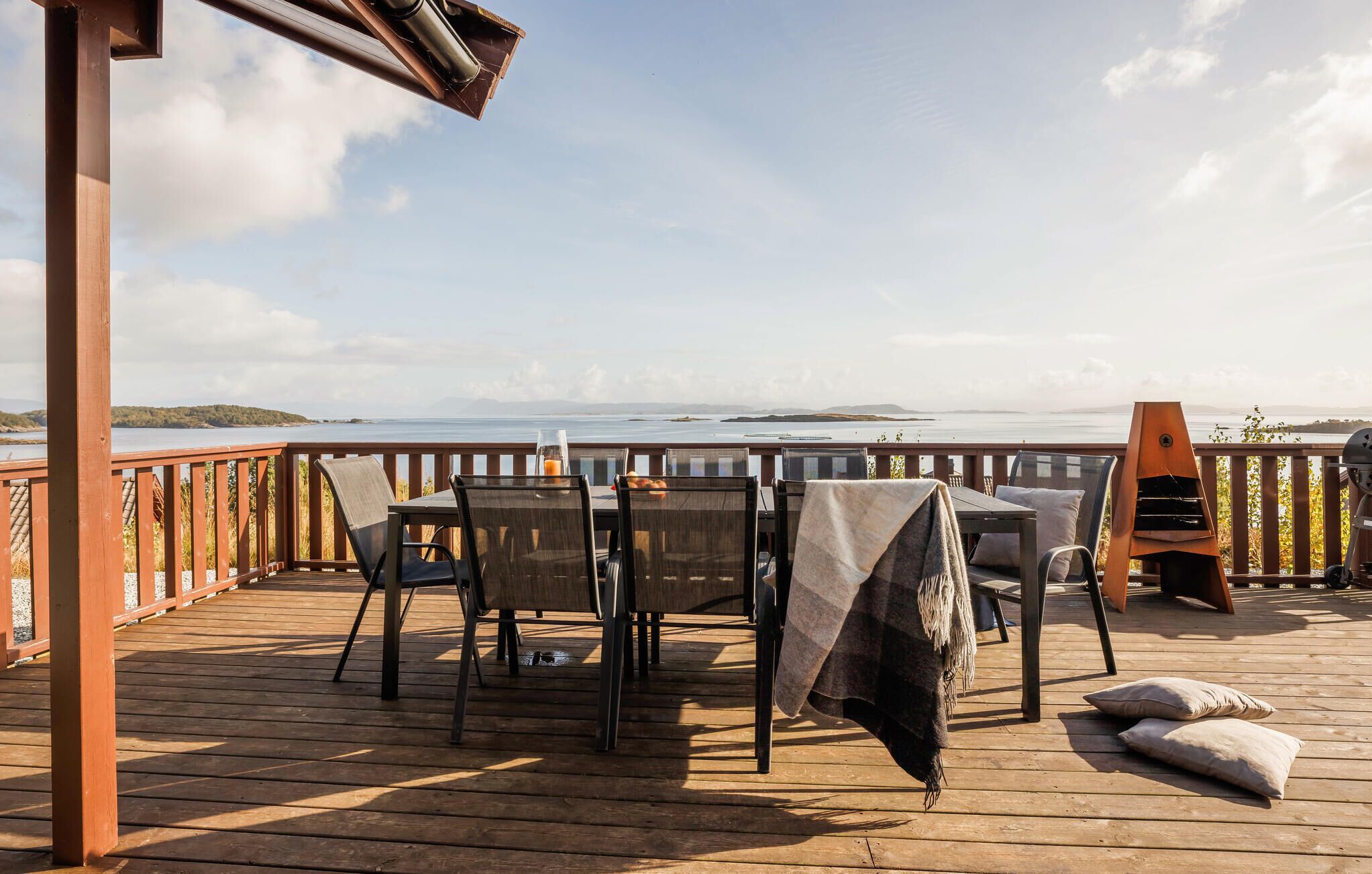 A wooden deck with a table and chairs, a grill, and a view of the water.