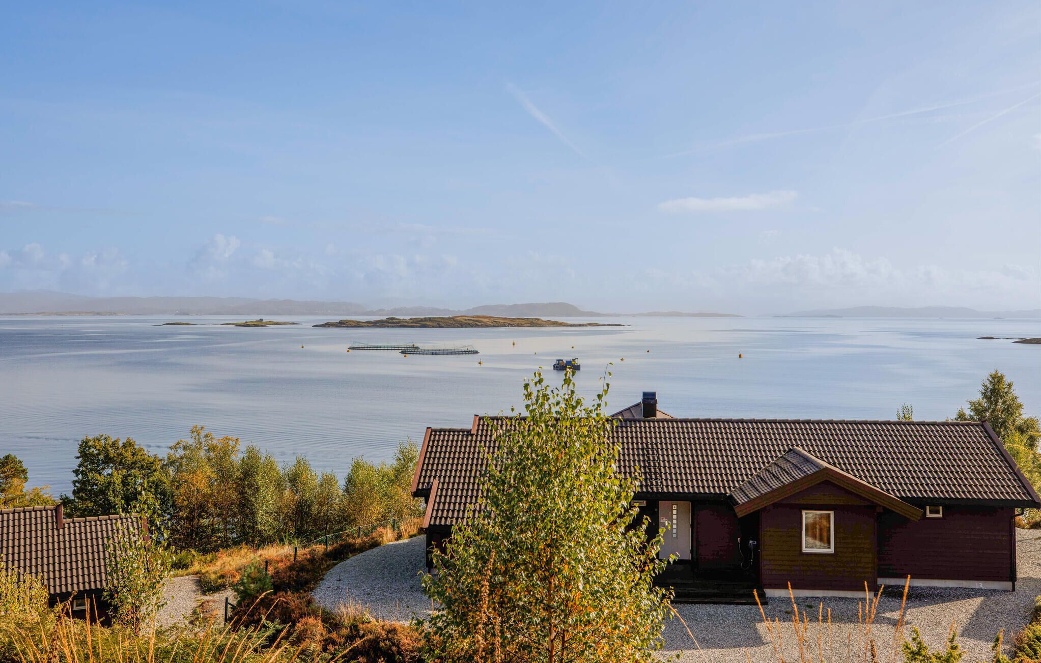 Une propriété située sur la côte, avec une maison dotée d’un toit en tuiles, entourée d’arbres et offrant une vue sur la mer.