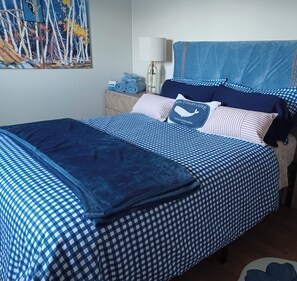 Una cama bien hecha con ropa de cama azul y blanca a cuadros, un cojín con diseño de ballena y un cuadro en la pared.