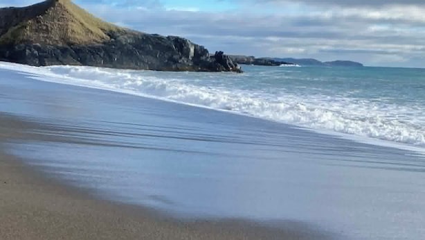 A beach with a rocky outcrop and calm waves. - Newfoundland’s Quiet Coast Calls (Harbour Breton)