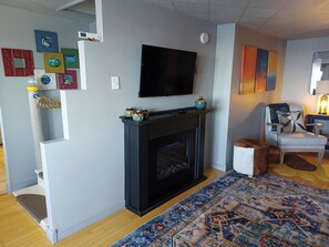 Una sala de estar con chimenea, un televisor montado en la pared, un tapete estampado y un sillón.