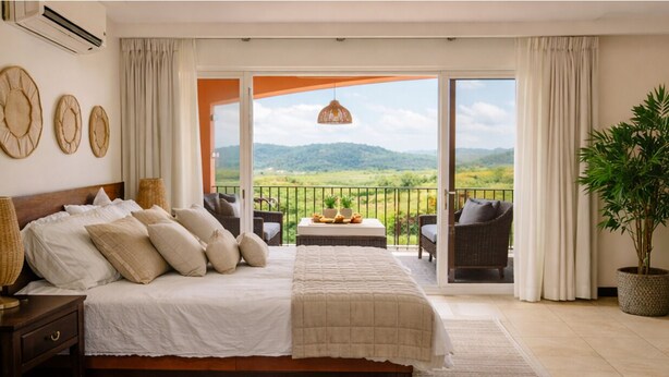 Ein Schlafzimmer mit einem großen Bett, einem Balkon mit Blick ins Grüne und einer Zimmerpflanze.