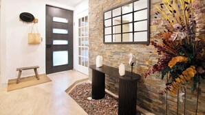 Een moderne lobby met een stenen muur, een zwarte deur, een bank en een decoratieve plantencompositie.