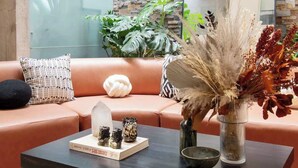 Een moderne woonkamer met een leren bank, een salontafel met decoratieve objecten, een vaas met gedroogde planten en een stenen muur met een raam erboven.