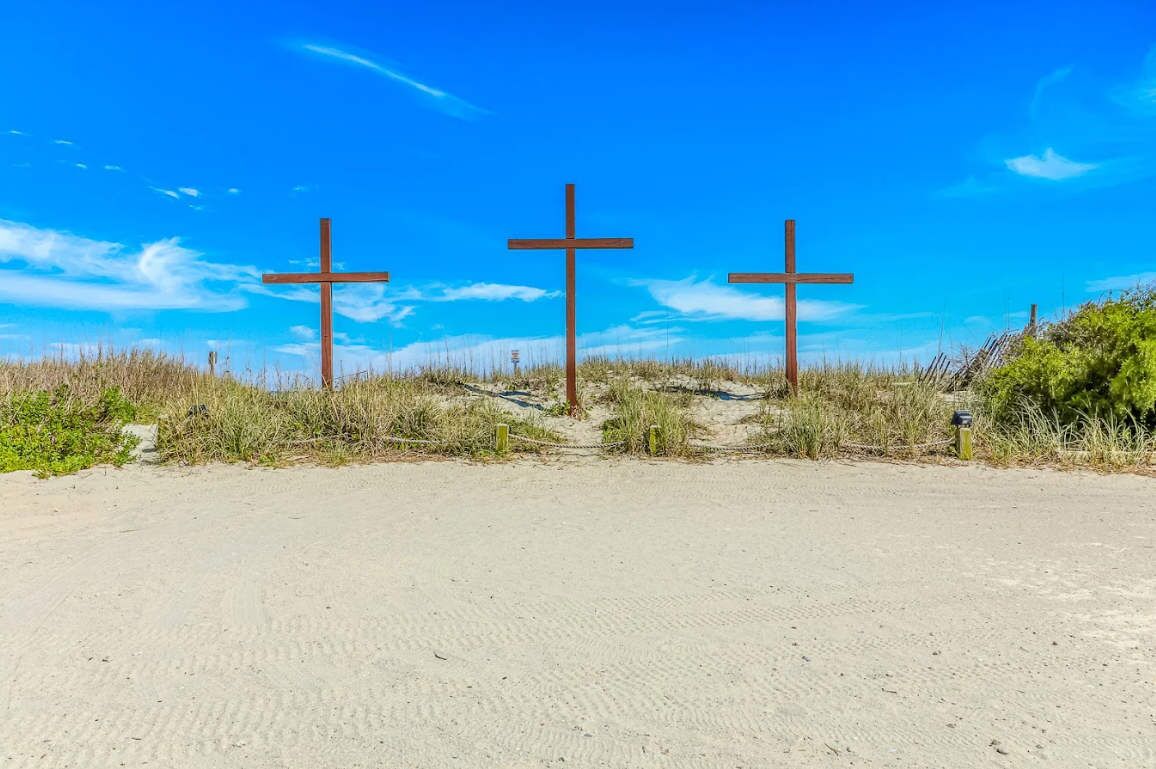 Three wooden crosses on a sandy beach with a clear blue sky.
