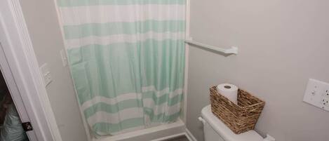 A bathroom with a shower curtain, toilet, and a basket of toilet paper.