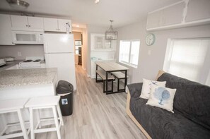 A compact kitchen with white cabinets, a microwave, and a stove. There's a dining area with a table and benches, and a gray sofa with decorative pillows. - Ocean Lakes 1586 (Myrtle Beach)