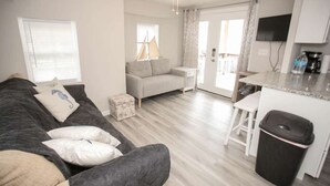 Un salon avec un canapé, une petite table et un coin cuisine comprenant un comptoir et une poubelle.