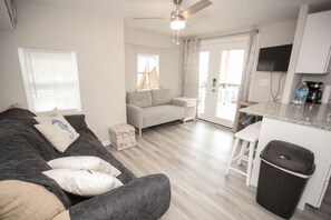 A living room with a sofa, a small table, a kitchen area with a counter and a trash bin. - Ocean Lakes 1586 (Myrtle Beach)