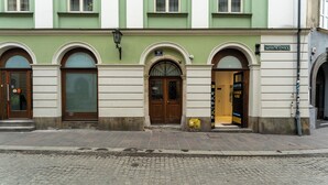 Un edificio con tre portali ad arco, un lampione e un cartello con su scritto "Mikojaška".