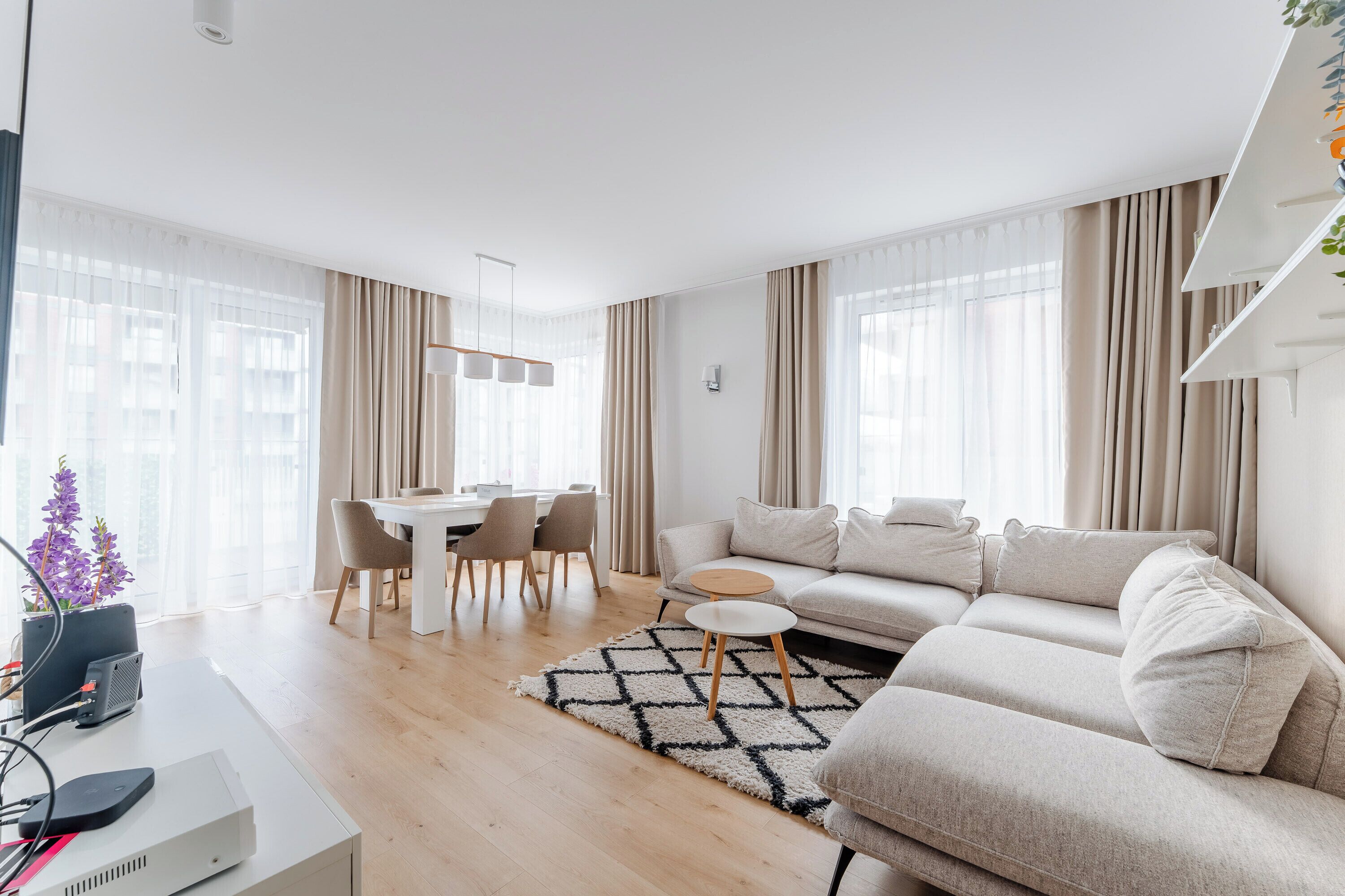 A modern living room with a sofa, a dining table with chairs, and a TV on a desk.
