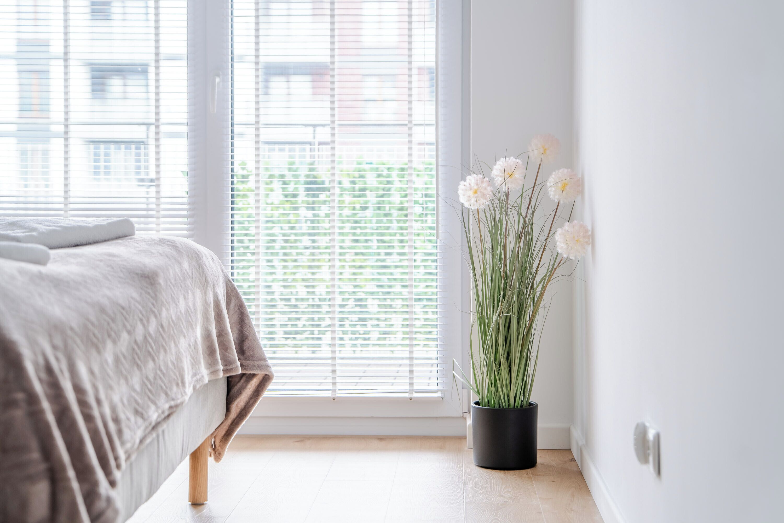 Et soveværelse med seng, et vindue med rullegardiner og en potte med blomster.