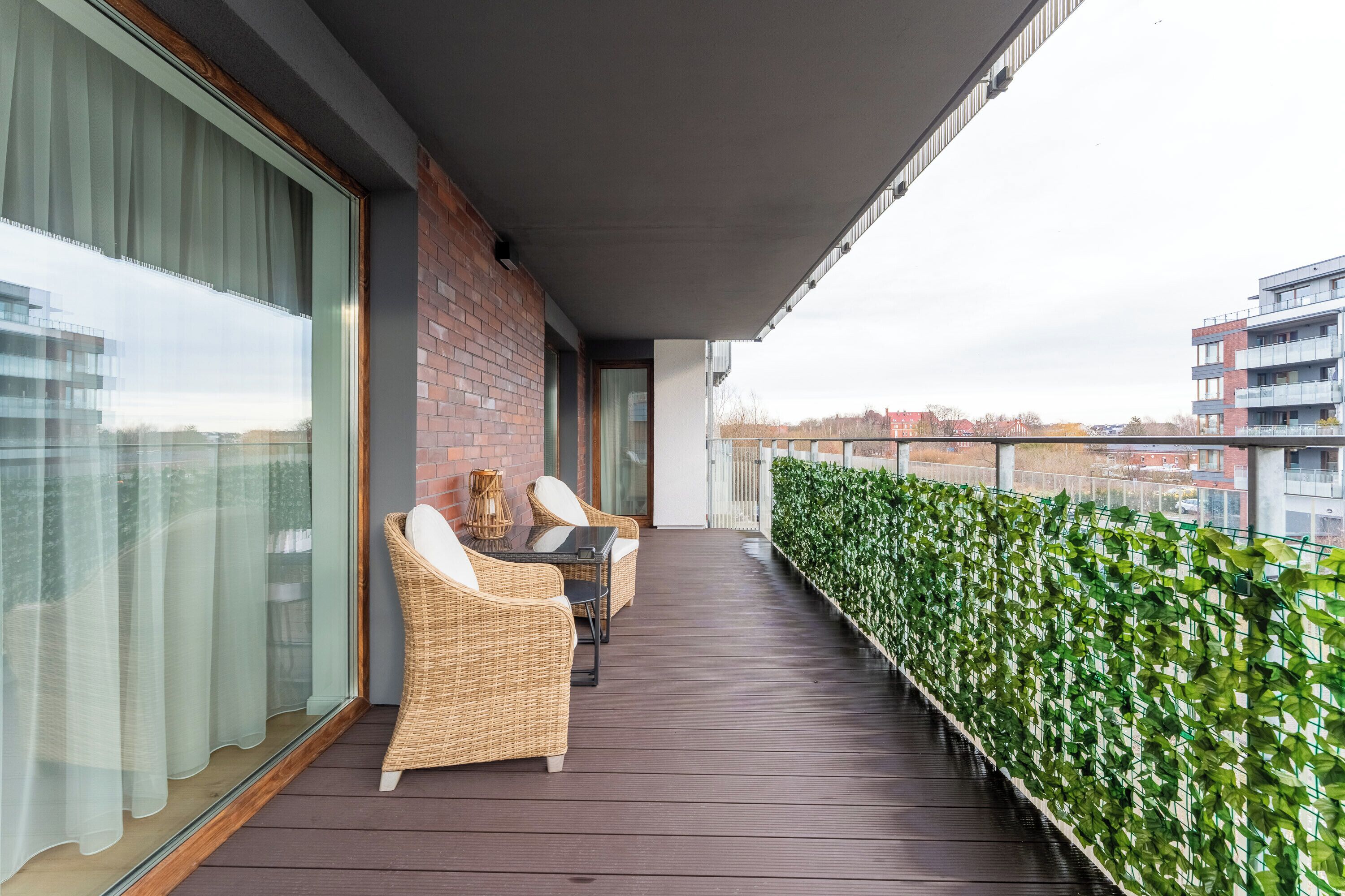 A balcony with wicker furniture, a glass table, and a view of the cityscape.