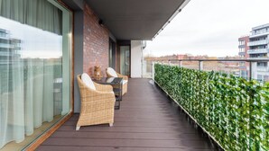 Ein Balkon mit Korbmöbeln, einem Glastisch und Blick auf die Stadtlandschaft.