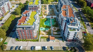 Eine Vogelperspektive zeigt einen modernen Wohnkomplex mit mehreren Gebäuden, einem zentralen Innenhof mit Swimmingpool und umgebender Bepflanzung.
