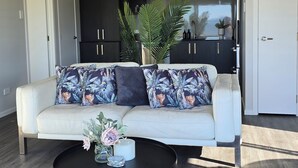 Een moderne woonkamer met een witte bank, een zwarte salontafel en een keuken op de achtergrond.