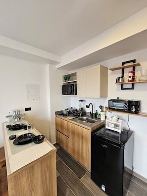 A compact kitchen with a microwave, toaster, and coffee maker on the countertop, a sink, and wooden cabinets. - InnerBloom Your loft in the best neighborhood in Medellín, just 5 minutes from the stadium. (Medellín)