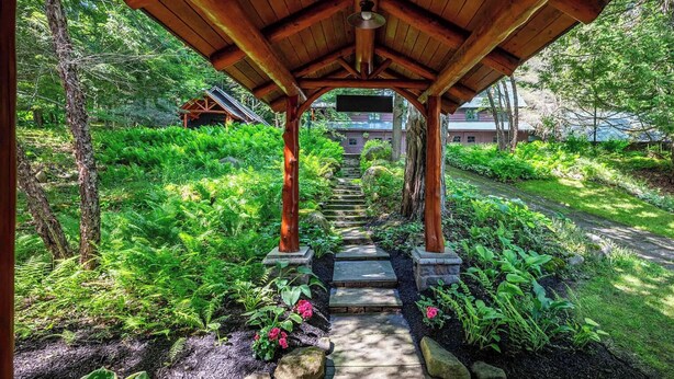 Una pérgola de madera con un camino de piedra que lleva a un edificio.