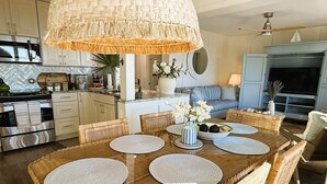 A dining area with a woven table and chairs, a hanging light fixture, and a kitchen in the background. - Oceanfront Sanctuary in Hilton Head Island (Hilton Head Island)
