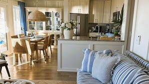 A modern kitchen with a central island, dining area with wicker chairs, and a striped sofa. - Oceanfront Sanctuary in Hilton Head Island (Hilton Head Island)
