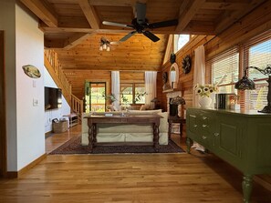 A spacious room with a wooden ceiling, a ceiling fan, a dining table, a sofa, a cabinet, and a television. - Grindelwald Cabin Mountain Retreat- Dog Friendly! (Maggie Valley)