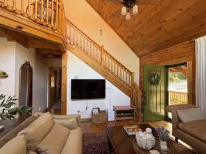 A wooden interior with a staircase, a flat-screen TV, a green door, and a beige sofa. - Grindelwald Cabin Mountain Retreat- Dog Friendly! (Maggie Valley)