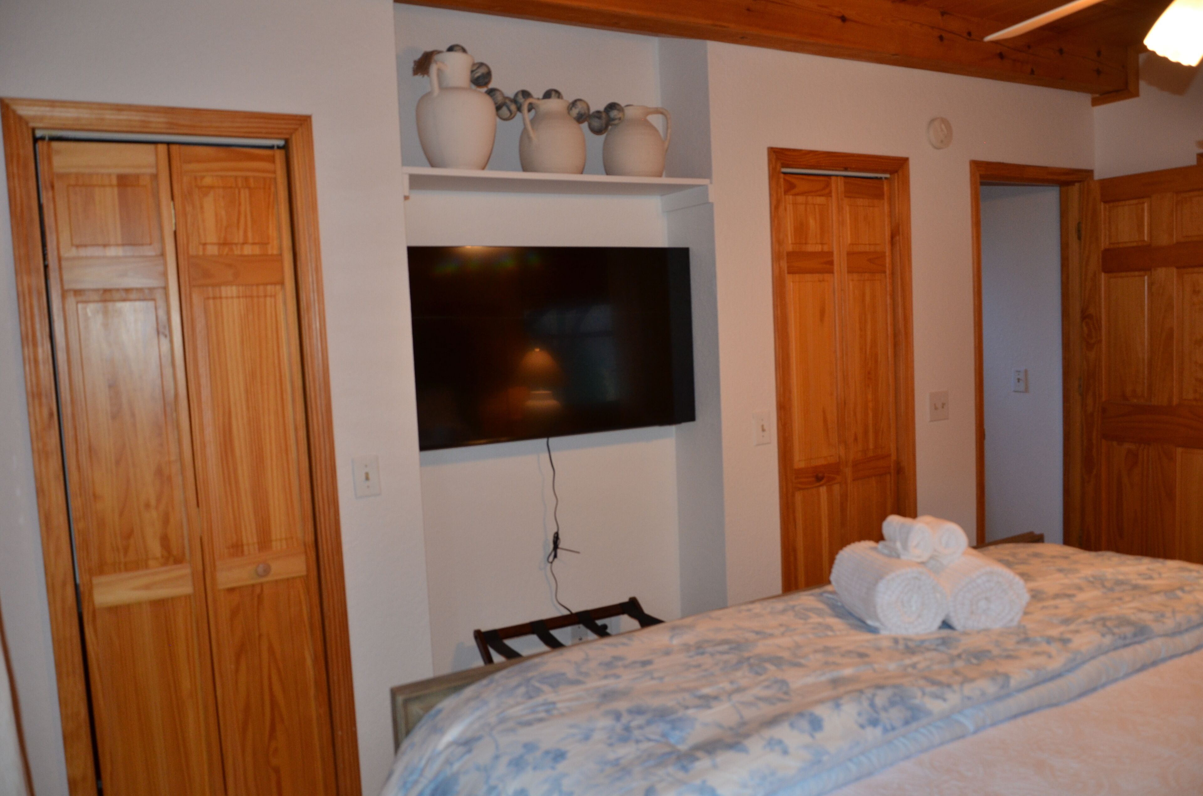 Una camera da letto con un letto, una TV a muro, porte in legno e uno scaffale con oggetti decorativi.