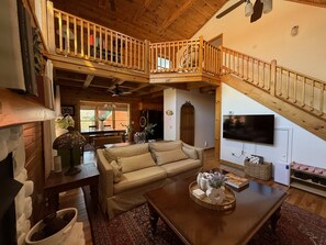 A spacious living area with a wooden staircase, a sofa, a coffee table, and a fireplace. - Grindelwald Cabin Mountain Retreat- Dog Friendly! (Maggie Valley)