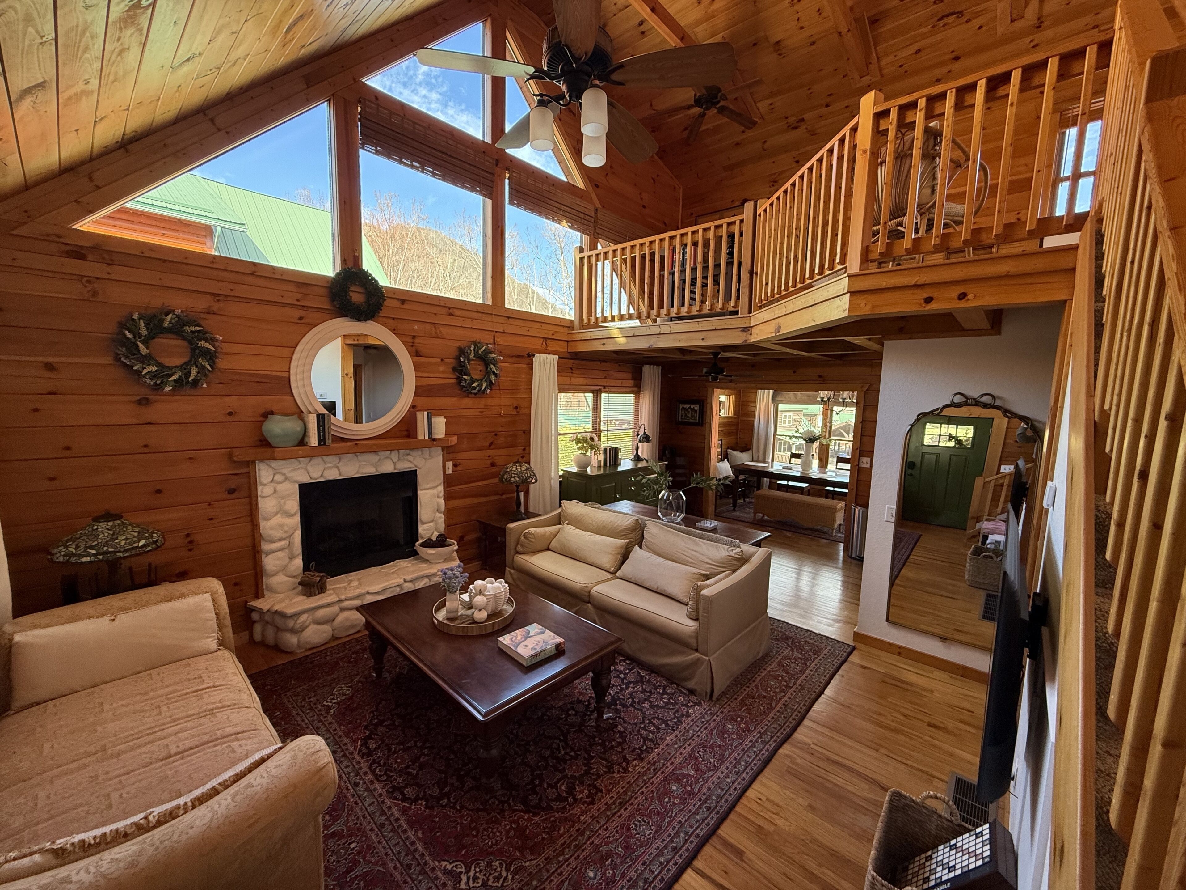 A spacious living room with a fireplace, a high ceiling with a balcony, and a view of the outside.