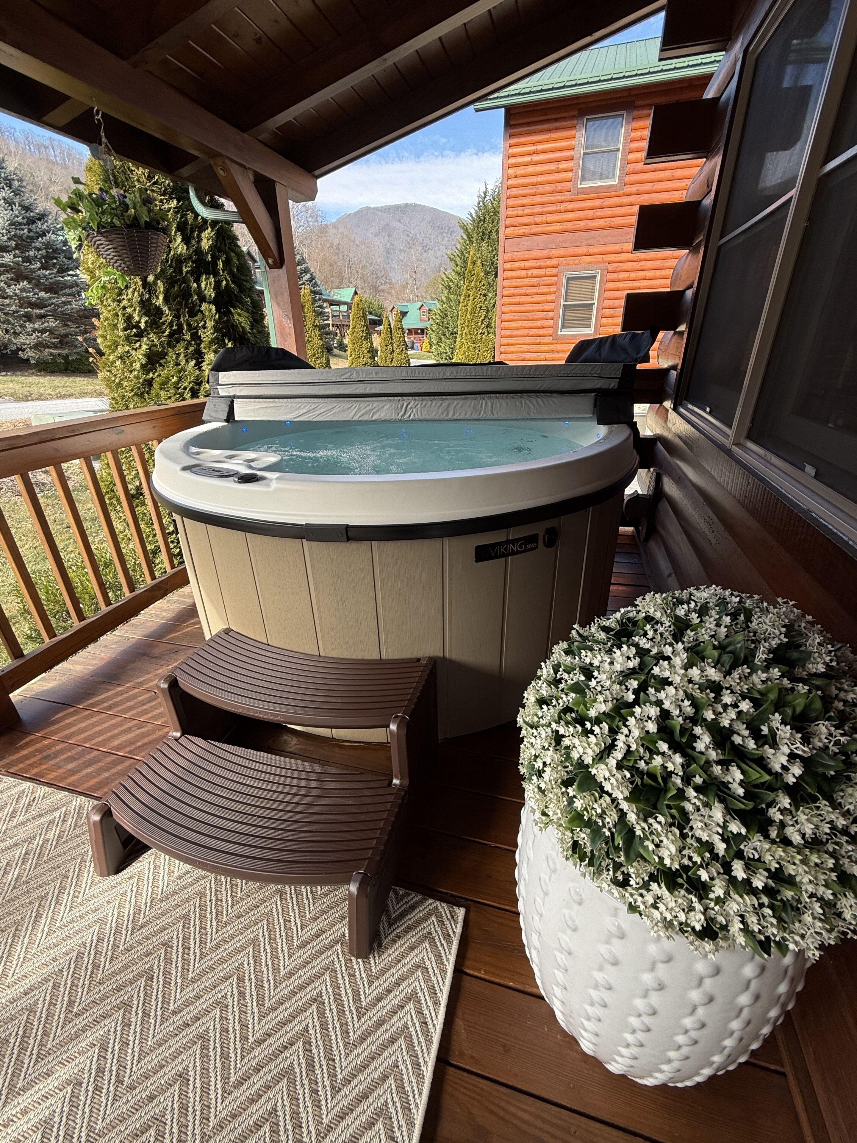 A wooden deck with a hot tub, two chairs, and a potted plant.