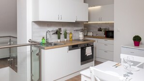 Ett modernt kök med vita skåp, en diskho i rostfritt stål och en bänkskiva i trä. Det finns en liten matplats med ett vitt bord och stolar.